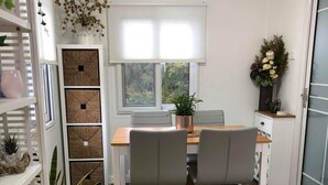 A modern kitchen with a dining area, featuring a wooden table, two chairs, and a potted plant. - The Cwtch - Cosy Home, with Breakfast Basket (Little Hartley)