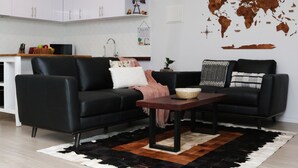 A modern living room with a black leather sofa, a wooden coffee table, and a world map wall decoration.