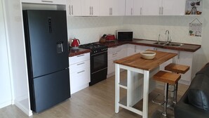 A modern kitchen with white cabinets, a black refrigerator, a gas stove, a microwave, and a wooden island with stools.