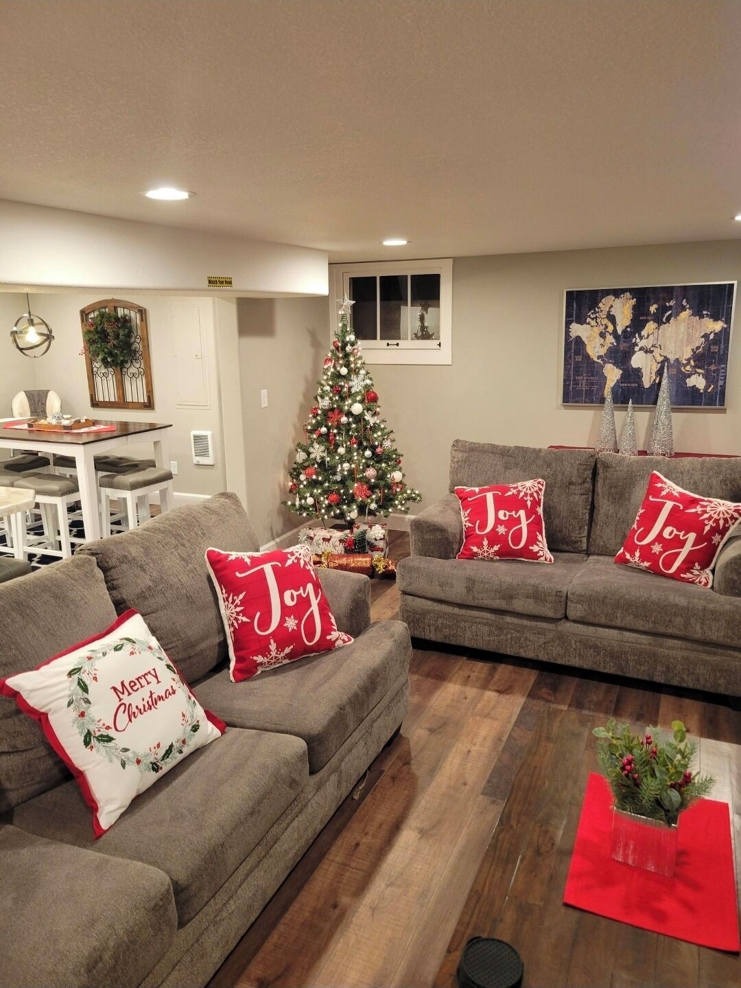 Un salon avec deux canapés gris, un sapin de Noël et des coussins décoratifs de fêtes.