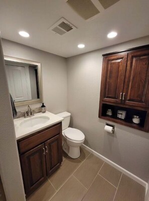 Une salle de bain avec un lavabo blanc, des meubles en bois, des toilettes et une étagère contenant des articles de toilette.
