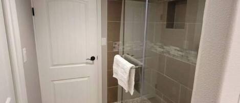 Une salle de bain avec une douche à parois de verre, une porte blanche et des carreaux de couleur beige.