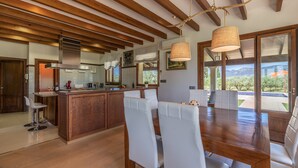 A modern kitchen with wooden beams, a central island, white chairs, and a dining table. - Modern finca, secluded location, 10min to the dream beach Playa del Muro, large pool (Búger)