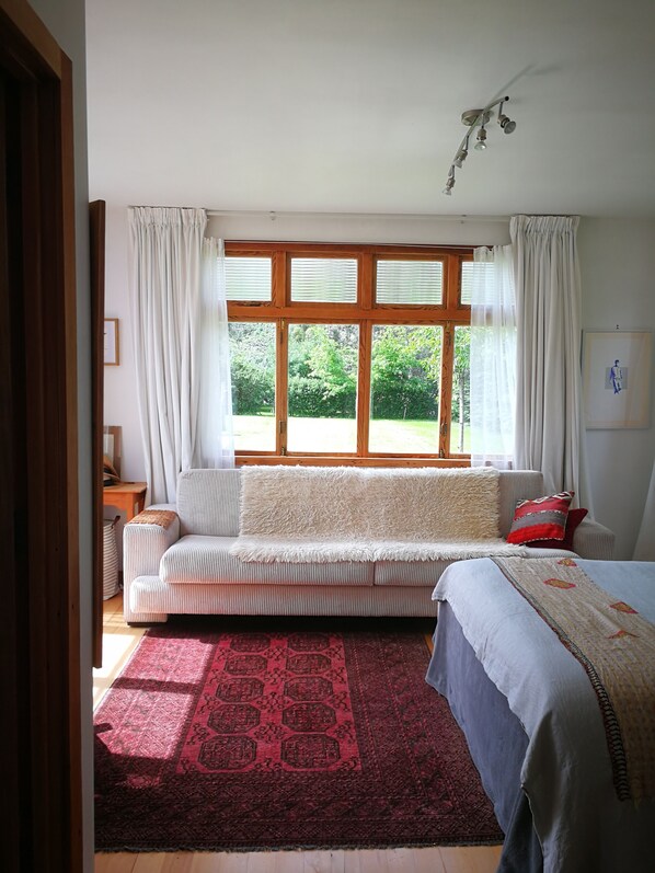 A room with a large window, a sofa, a bed, and a rug.