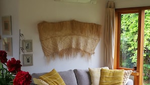 Uma sala de estar acolhedora com um sofá, uma mesa de centro de madeira com frutas e uma janela grande com vista para o verde.