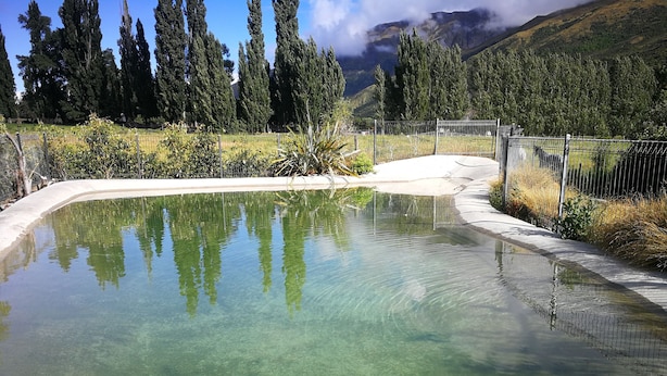 Piscina transparente com cerca ao redor, cercada por vegetação e montanhas ao fundo.