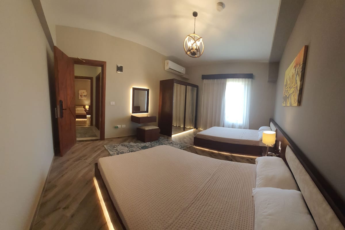 A hotel room with two beds, a mirror, a wardrobe, an air conditioning unit, and a chandelier.