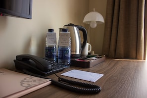 A hotel room desk with a telephone, two bottles of Aquafina water, a kettle, a lamp, and a notepad.
