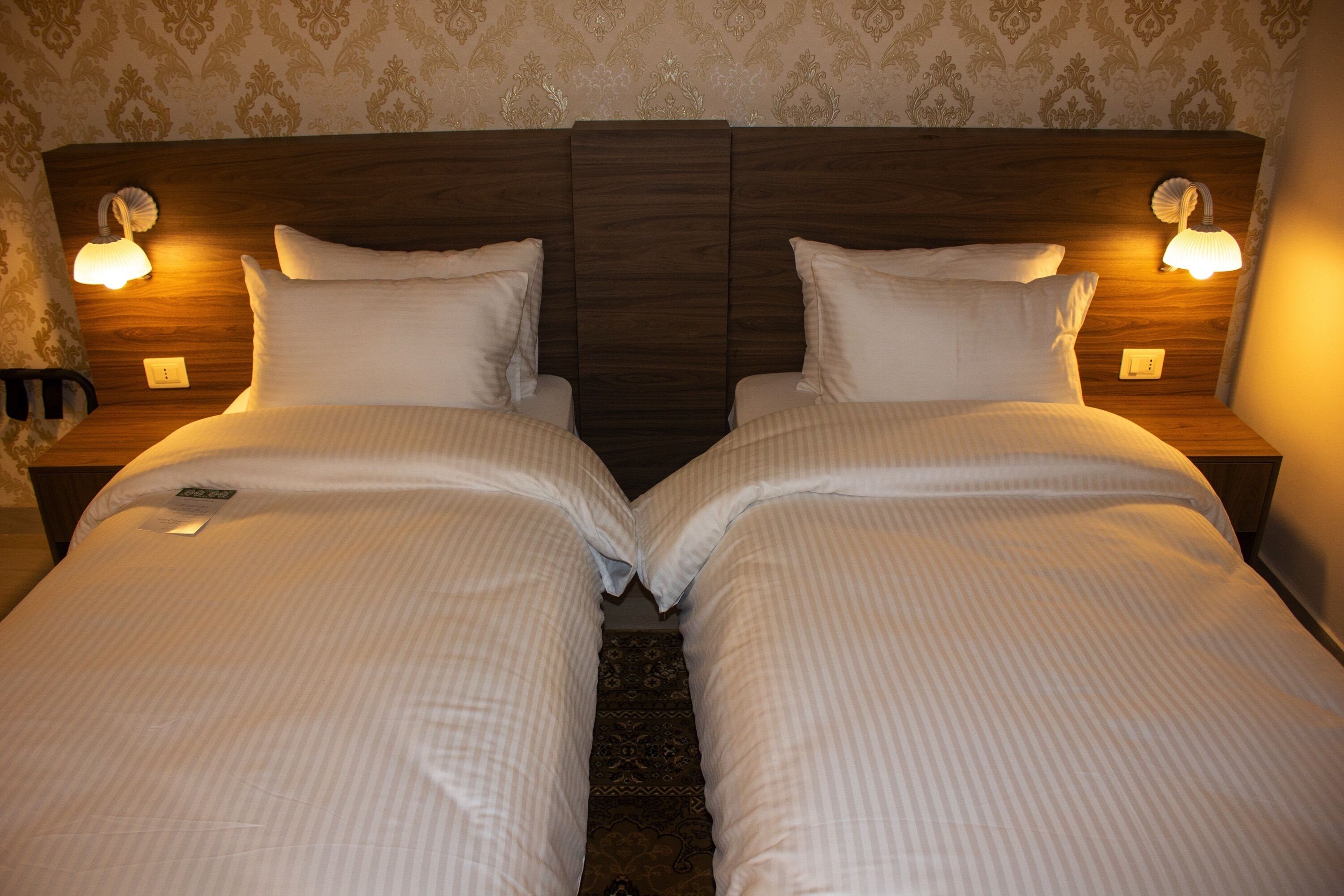 A double bed with a wooden headboard, two bedside lamps, and a decorative wall pattern.