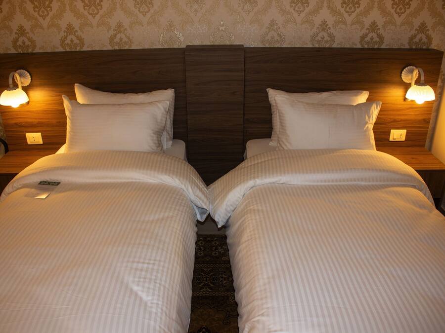 A double bed with a wooden headboard, two bedside lamps, and a decorative wall pattern.