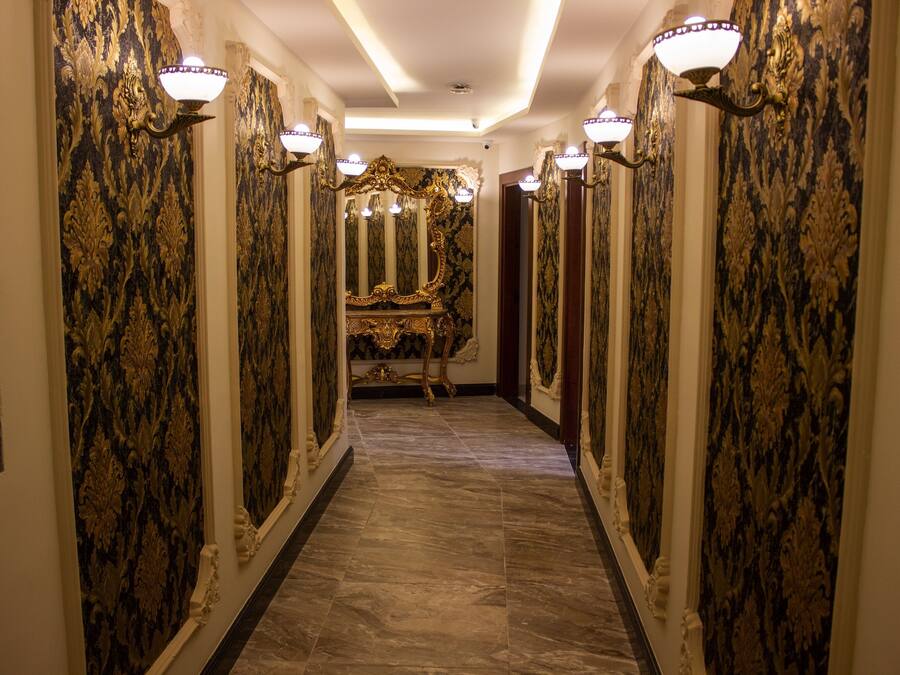 A hallway with ornate wallpaper, a marble floor, and wall sconces.