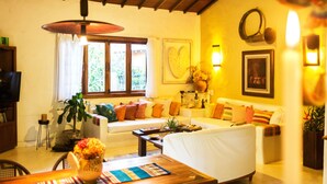 A cozy living room with a sofa, a coffee table, and a dining table with a vase of flowers. - Beautiful house with 4 suites and swimming pool in Trancoso (sleeps 10 people) (TRANCOSO)