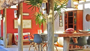 An outdoor dining area with wooden tables and chairs, surrounded by potted plants and a red wall. - Beautiful house with 4 suites and swimming pool in Trancoso (sleeps 10 people) (TRANCOSO)