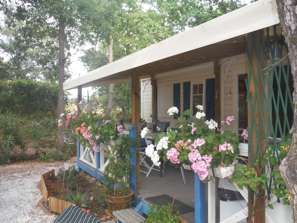 A covered porch with a wooden bench, a table, and potted plants.