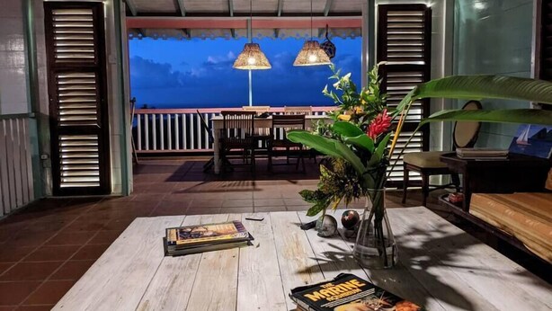 Ein Zimmer mit einem Holztisch, zwei Pendelleuchten, einem Blumentopf und Blick auf den Ozean.