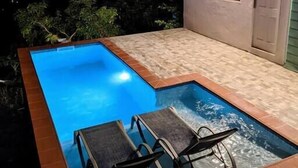 Ein rechteckiger Pool mit einer gefliesten Liegefläche, umgeben von einem roten Sonnensegel.
