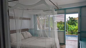 Ein Schlafzimmer mit Baldachinbett, einem Fenster mit Jalousien und Blick ins Grüne.