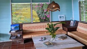 Ein Zimmer mit einer hölzernen Bank, einem Tisch mit Büchern und einer Pflanze, sowie einer hängenden Leuchte.