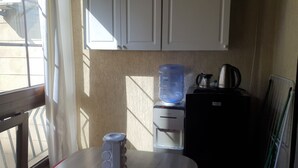 A kitchen with white cabinets, a water dispenser, a kettle, and a refrigerator. - Cosy studio. (Mansourieh)