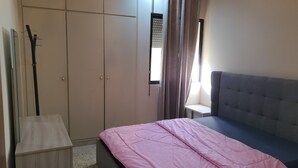 A bedroom with a bed, a wardrobe, a window with curtains, and a bedside table. - Cosy studio. (Mansourieh)