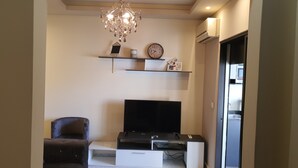 A living room with a flat-screen TV, a sofa, a chandelier, and wall-mounted shelves with decorative items. - Cosy studio. (Mansourieh)