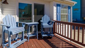 Une terrasse en bois avec deux chaises Adirondack et une table, un bâtiment blanc avec des volets bleus, et un bâtiment bleu portant une enseigne indiquant « Hyperion Towers ».