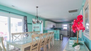 Une cuisine moderne avec des meubles blancs, une table à manger en verre et un luminaire suspendu.