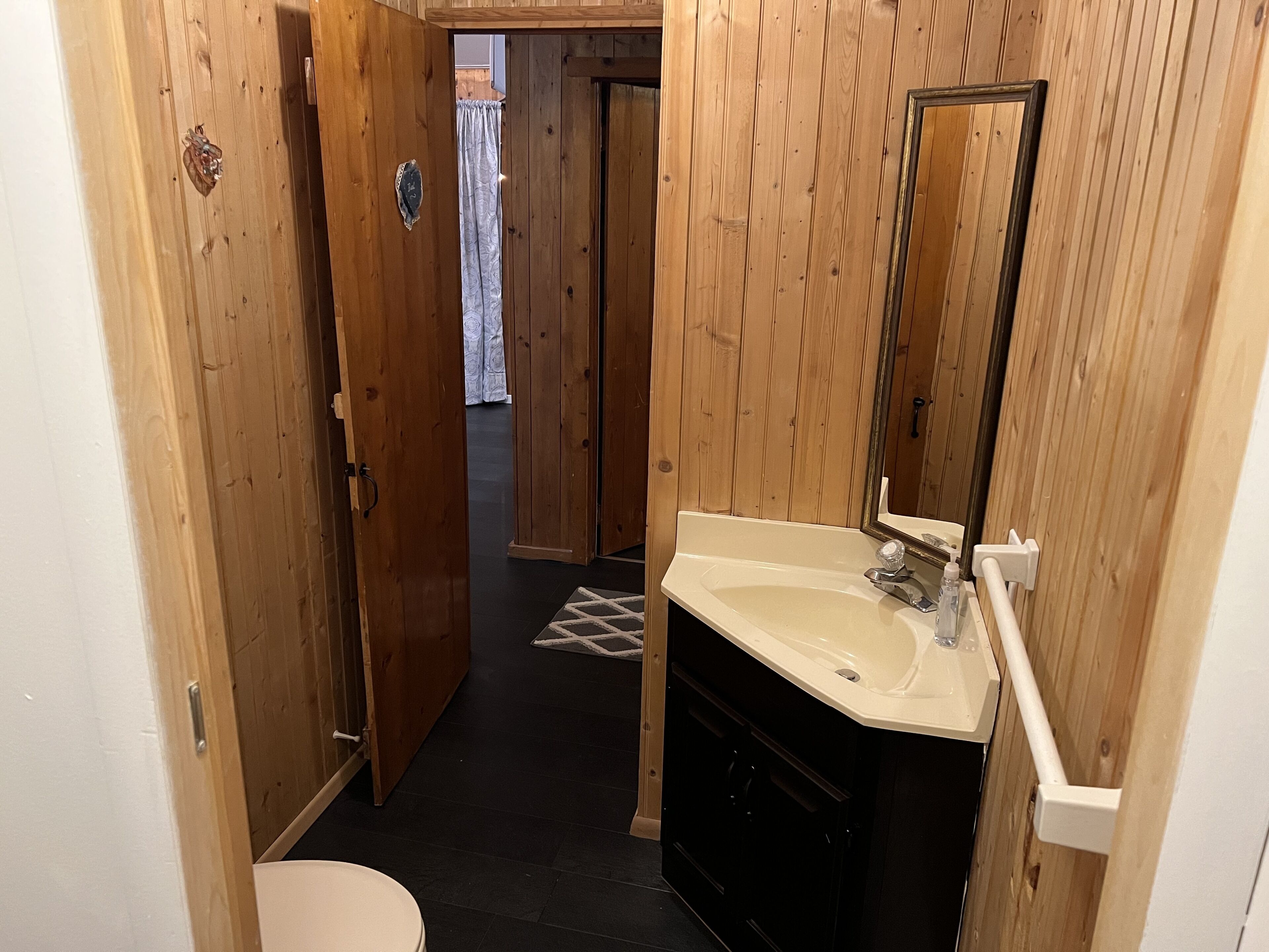 Un baño con paneles de madera, un lavamanos blanco, un espejo y un inodoro.