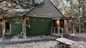 A small green building with a porch, a bench, and a wheelbarrow.