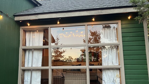 A multi-pane window with curtains, a wooden bench, and string lights.