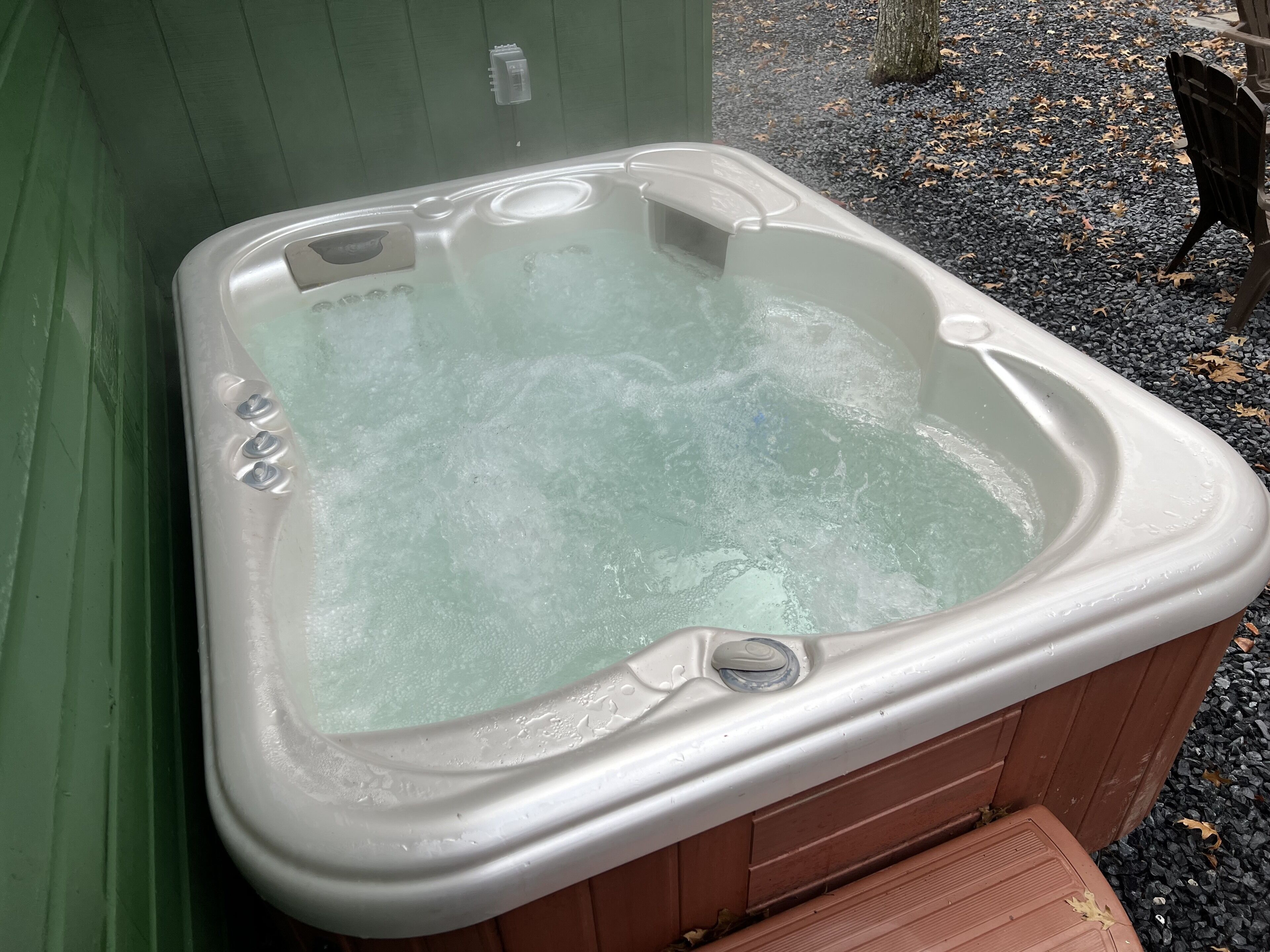 A hot tub with a wooden exterior, a control panel, and a small step leading into it.