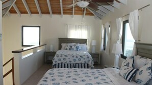 A bedroom with two beds, a wooden ceiling, a window with curtains, and a nightstand with a lamp.