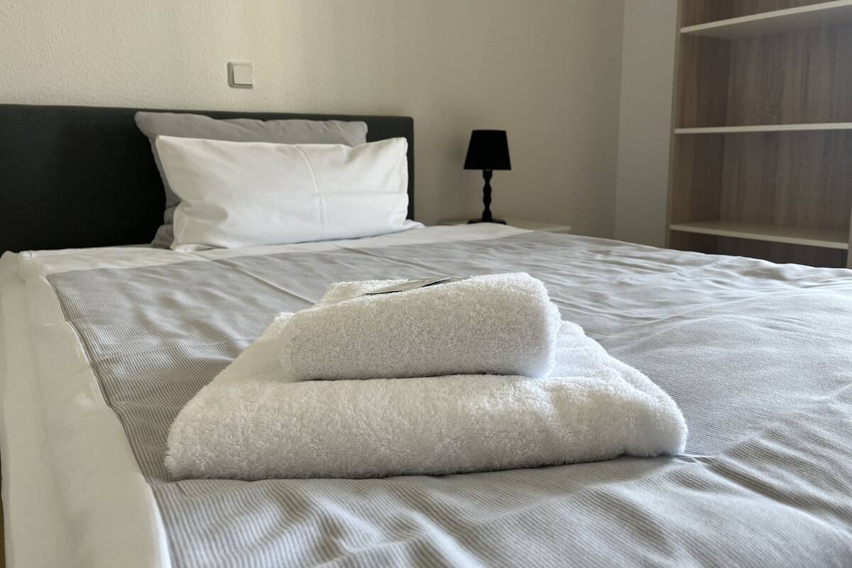 A neatly made bed with white linens and two folded towels.