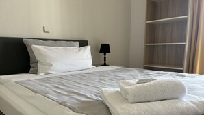Ein ordentlich bezogenes Bett mit weißen Laken, ein gefaltetes weißes Handtuch und eine Nachttischlampe.