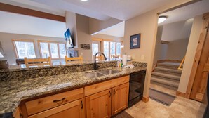A kitchen with granite countertops, wooden cabinets, a stainless steel sink, and a built-in oven. There is a dining area with wooden chairs and a table, and a staircase leading to another level.