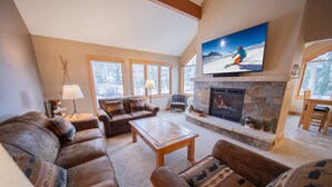 A cozy living room with leather sofas, a stone fireplace, and a large TV mounted above it.