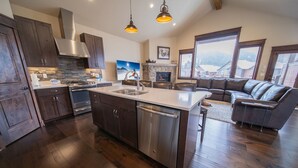 A spacious kitchen with dark wooden cabinets, stainless steel appliances, and a central island with a dishwasher. - Updated Townhome | Private Hot Tub | Pool access (Keystone)