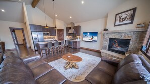 A modern living room with a large brown leather sofa, a wooden coffee table, and a stone fireplace. - Updated Townhome | Private Hot Tub | Pool access (Keystone)