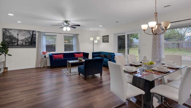 A spacious living room with a blue sofa, a dining area with a glass table, and a ceiling fan.