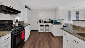 A modern kitchen with white cabinets, a black stove, and a wooden floor.