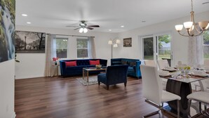 A spacious living room with a blue sofa, a dining table set for four, and a ceiling fan.