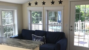 Sala de estar com um sofá azul escuro, bancada de pedra e porta que dá para área externa com cerca branca.