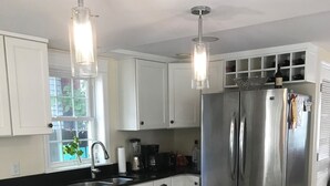 Cozinha moderna com armários brancos, geladeira de aço inoxidável, bancada de mármore e duas luminárias pendentes.