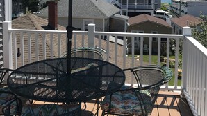 Um pátio com mesa, cadeiras, um guarda-sol e vista para as casas e o oceano.