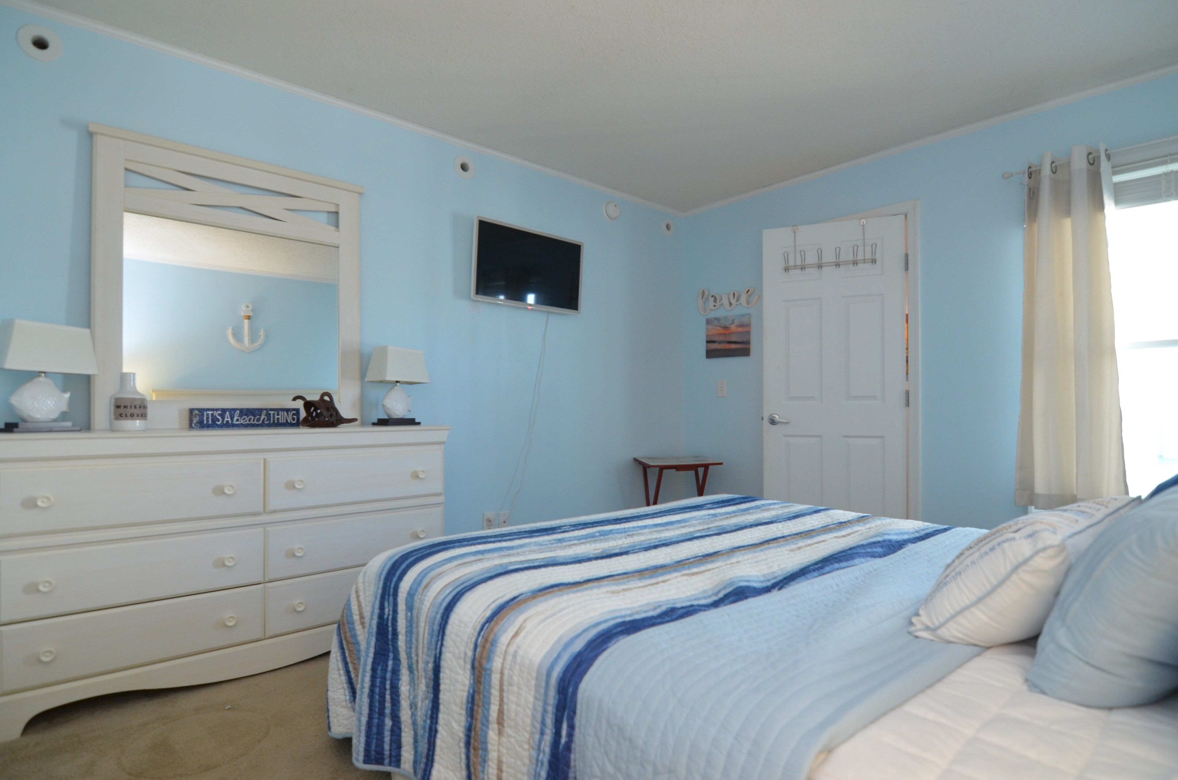 Une chambre à coucher avec un lit, une commode et un téléviseur fixé au mur.