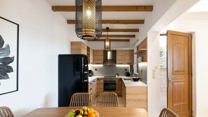 A modern kitchen with wooden cabinets, a black refrigerator, and a dining area with a wooden table and chairs. - Zen play apartment,pool,Near beach & amenities (Nea Magnisia)