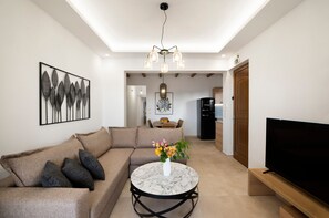 Un soggiorno moderno con un divano componibile, un tavolino rotondo con un vaso di fiori, una televisione a schermo piatto e un'area pranzo sullo sfondo.