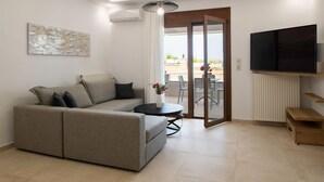 Un salon moderne avec un canapé gris, une table basse ronde, un téléviseur à écran plat et une porte-fenêtre coulissante donnant sur un espace extérieur.
