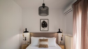 Un lit bien fait, agrémenté d’un coussin à motifs, de deux lampes de chevet, d’une œuvre d’art représentant des feuilles accrochée au mur et d’un luminaire suspendu.