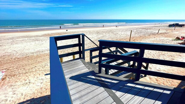 A wooden boardwalk leading to a beach with clear skies and calm waters.